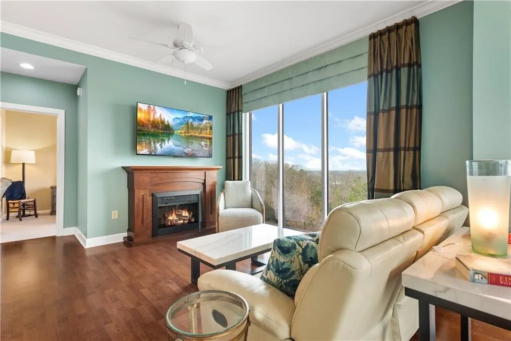 Living area with a warm lit fireplace, a ceiling fan, wood finished floors, and crown molding