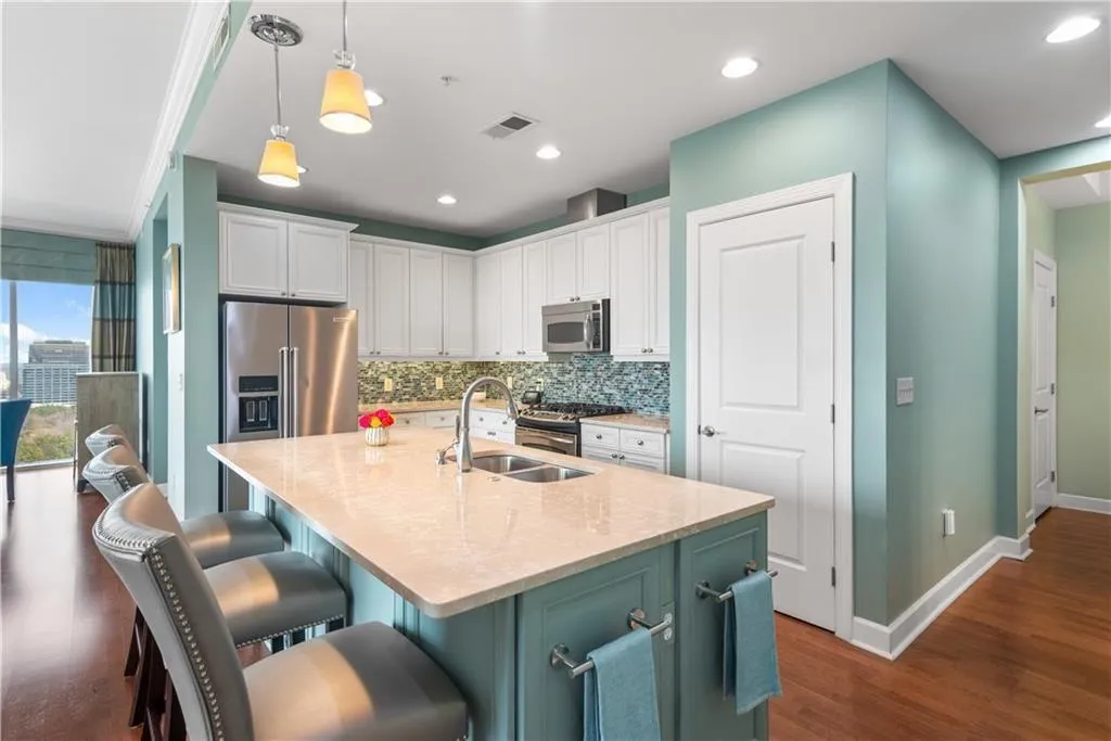 Two tone kitchen featuring dual tone cabinetry, light stone counters, an island with sink, pendant lighting, and a breakfast bar