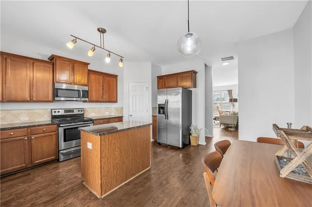 Kitchen with stainless steel appliances, a kitchen island, brown cabinets, backsplash, and dark wood finished floors