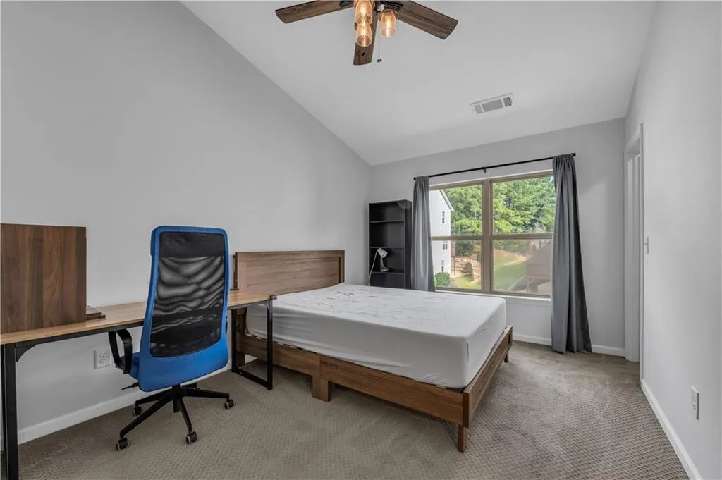 Carpeted bedroom featuring vaulted ceiling, ceiling fan, and an office area