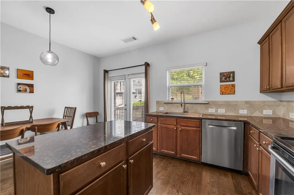 Kitchen with stainless steel appliances, dark wood-style floors, dark stone countertops, pendant lighting, and backsplash