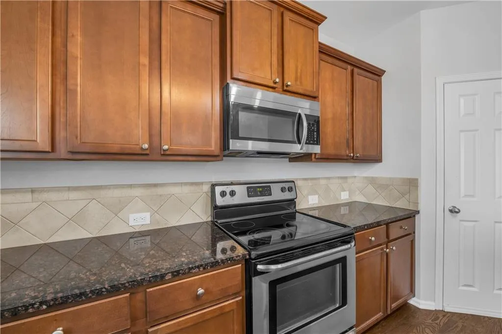 Kitchen featuring appliances with stainless steel finishes, tasteful backsplash, brown cabinetry, and dark stone countertops