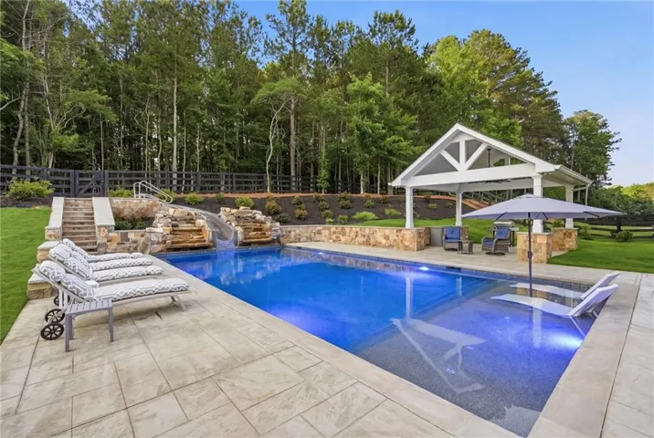 Resort-style pool area featuring a built-in slide, multiple waterfalls, and extensive paver decking
