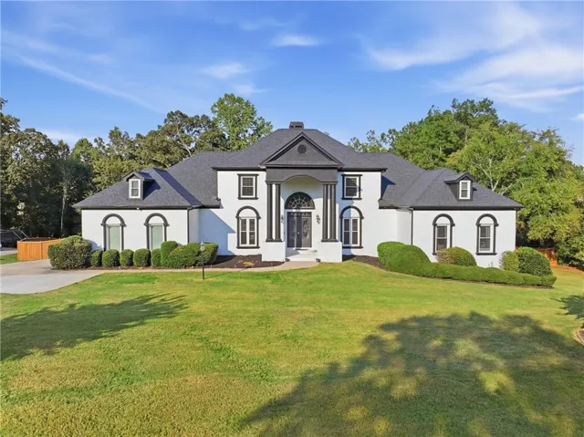 White exterior with black trim, a prominent portico, dark roofing, and dormer windows