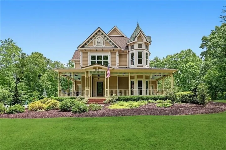Victorian-style exterior with a wraparound porch, turret, decorative gables, and mature landscaping