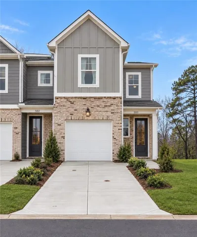 Townhome exterior featuring brick and vertical siding, a two-car concrete driveway, an attached garage, and a black front door with decorative glass