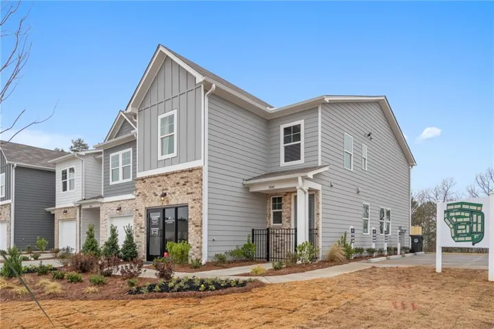 Multi-story townhome with light gray horizontal siding, vertical board and batten accents, and a brick facade