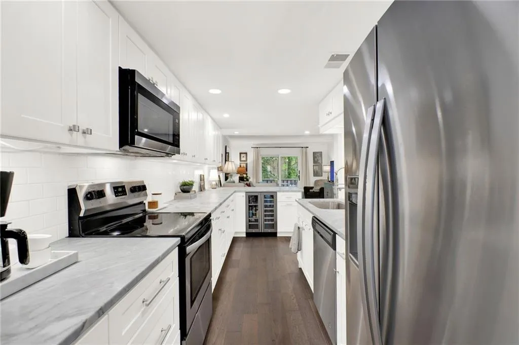 Kitchen featuring appliances with stainless steel finishes, beverage cooler, recessed lighting, dark wood finished floors, and light stone countertops