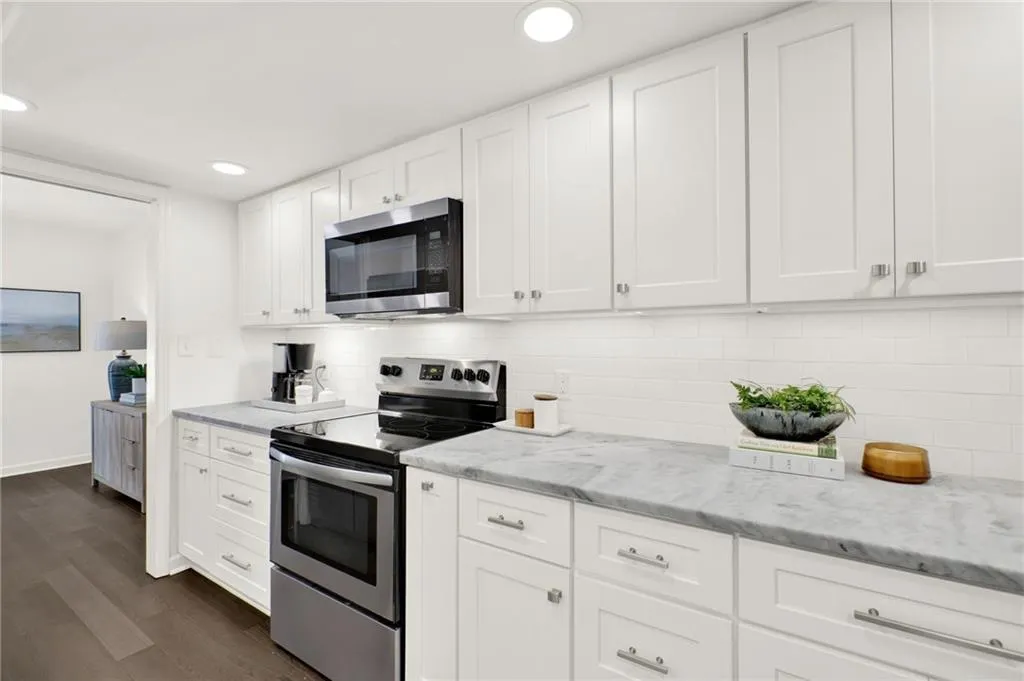 Kitchen featuring appliances with stainless steel finishes, dark wood-type flooring, white cabinetry, light stone counters, and recessed lighting
