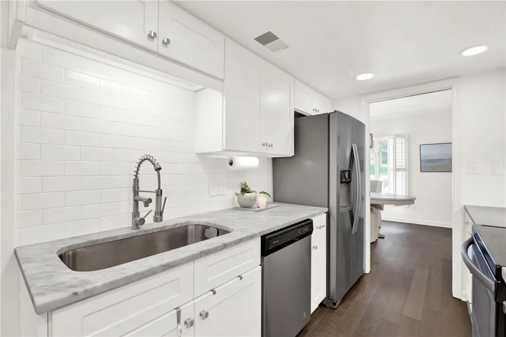 Kitchen featuring stainless steel appliances, white cabinets, tasteful backsplash, light stone countertops, and dark wood finished floors