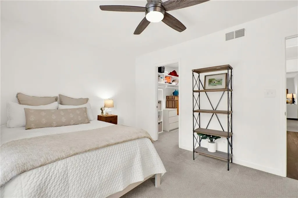 Bedroom featuring light carpet, a spacious closet, and a ceiling fan