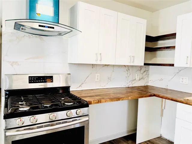 Kitchen with stainless steel gas range oven, butcher block counters, extractor fan, white cabinets, and open shelves