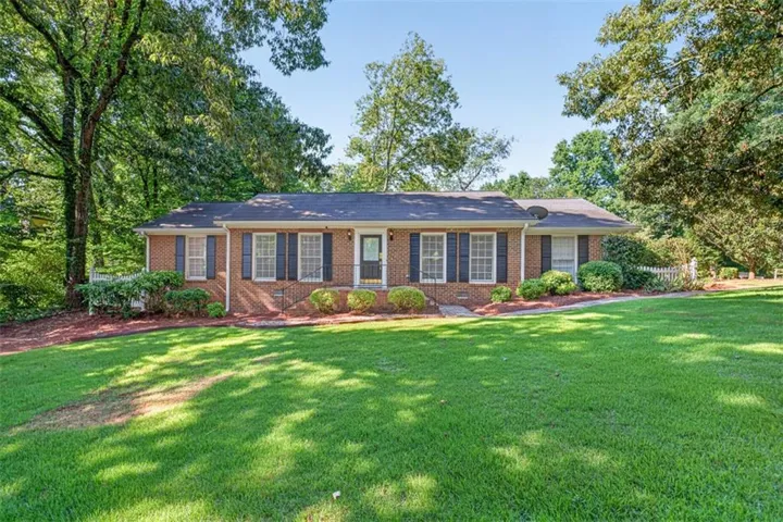Brick ranch home featuring a dark shingle roof, black louvered shutters, and a front entry with a storm door
