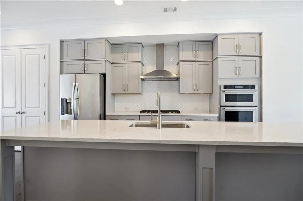 Kitchen featuring light stone countertops, wall chimney exhaust hood, appliances with stainless steel finishes, and gray cabinets