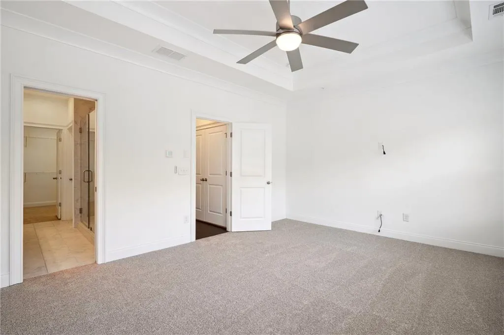 Unfurnished bedroom featuring ceiling fan, carpet, and a tray ceiling