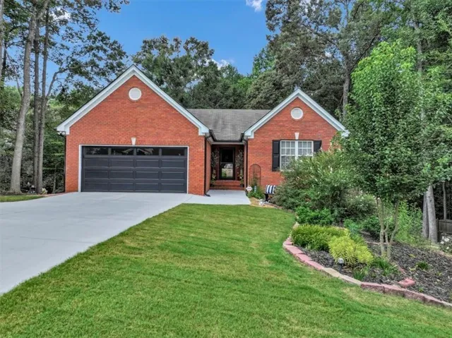 Charming brick residence with a two-car garage featuring dark panel doors, manicured front lawn, and established landscaping with mature trees
