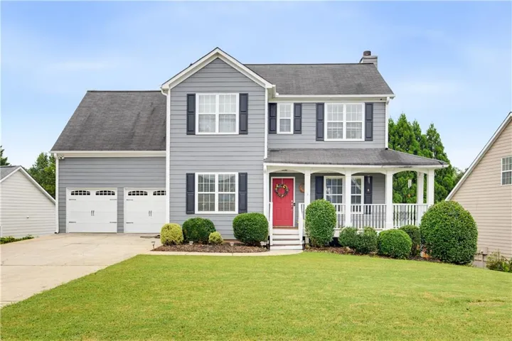 Two-story residence featuring light gray siding, dark shutters, a covered front porch, and an attached two-car garage