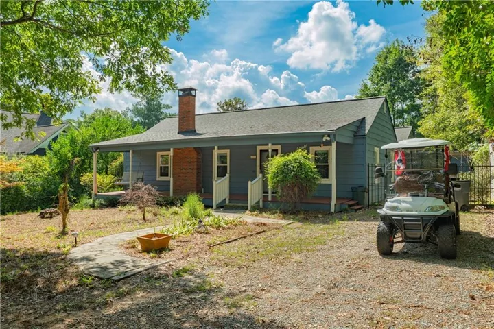 Single-story residence featuring a covered front porch, brick chimney, and a gravel driveway
