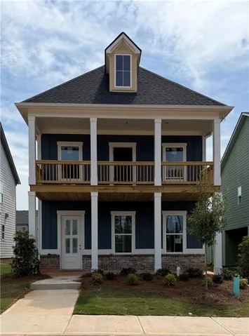 Two-story facade with a prominent dormer, covered porch, second-story balcony with wood railing, and brick accent foundation
