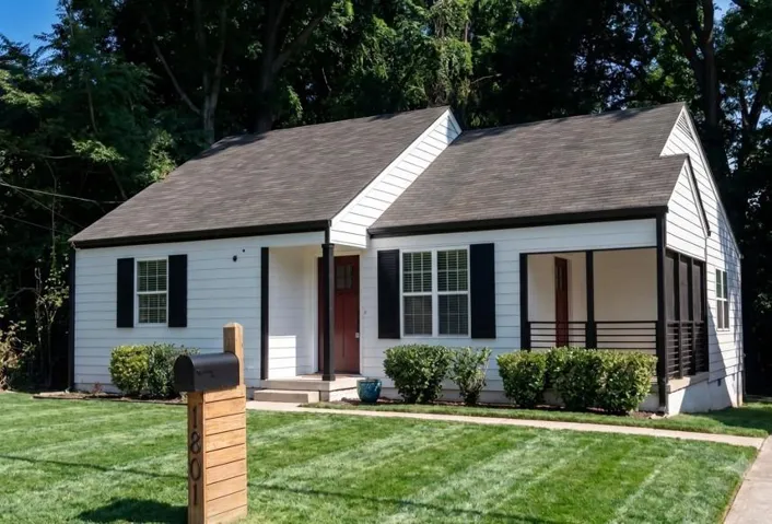 Exterior featuring white siding, black shutters, a dark shingle roof, and a covered front porch with dark railings