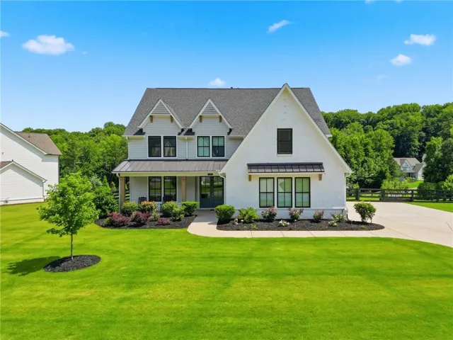 Modern farmhouse exterior with white brick and siding accents, featuring a dark shingle roof and black-framed windows