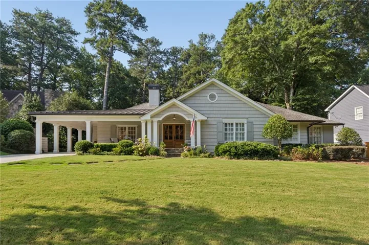 Gable roofline with shingle siding, covered front entry, portico with white columns, light-colored window shutters, and a manicured lawn