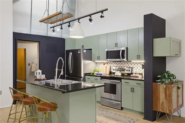Kitchen featuring sage green cabinetry, black countertops, stainless steel appliances, and a geometric pattern backsplash