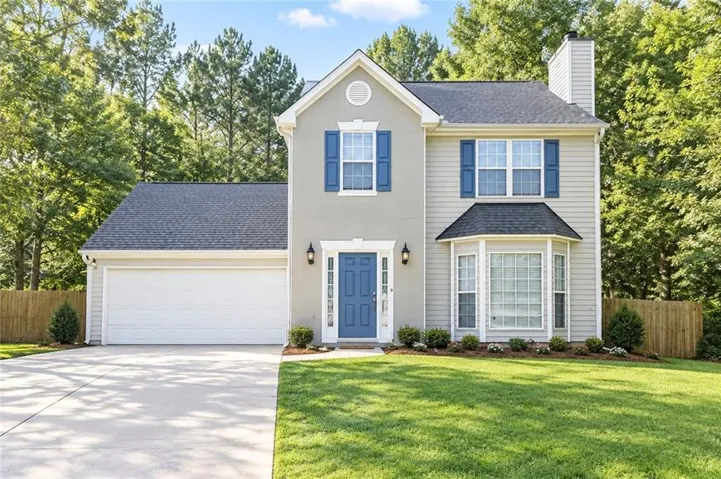 Two-story home featuring a bay window, attached garage, paved driveway, and mature landscaping