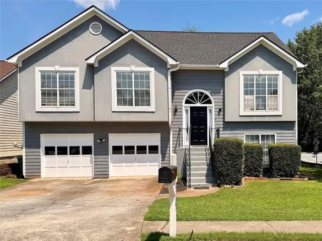 Grey two-story residence featuring a two-car garage with white paneled doors, a prominent black front door with an arched transom window, and a shingled roof