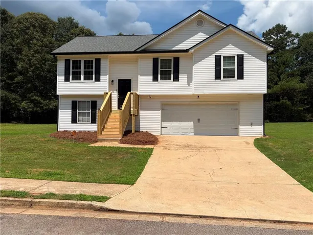 Two-story home featuring crisp white vinyl siding and black shutters, anchored by a two-car garage with concrete driveway