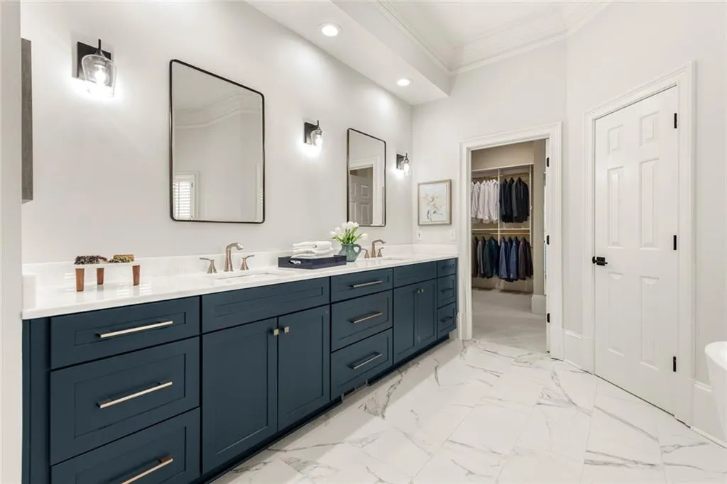 This elegant primary bath features custom cabinetry, dual sinks, and marble countertops, offering both style and functionality. A convenient view toward the walk-in closet enhances the flow and everyday ease of the space.