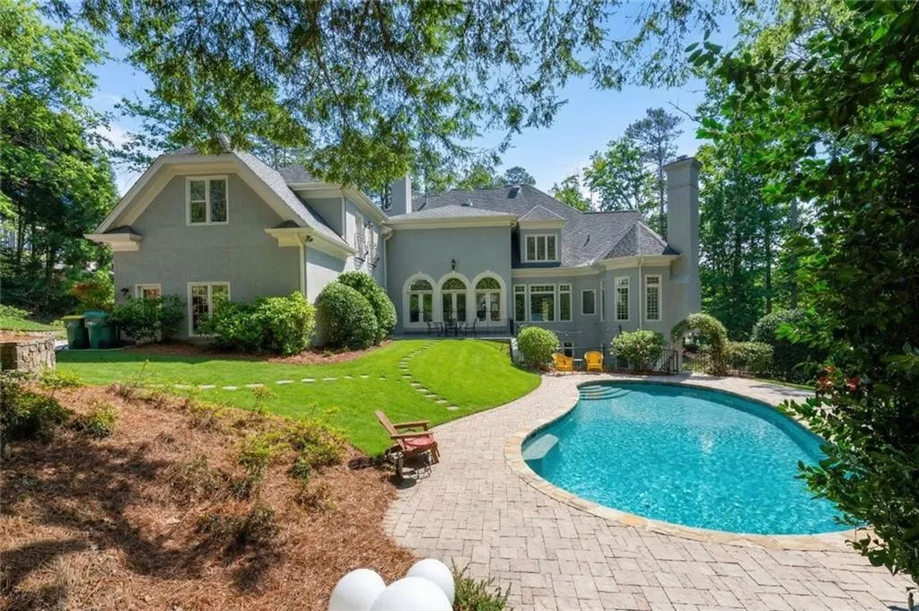 This inviting backyard retreat features a sparkling pool framed by lush landscaping and a spacious patio, perfect for outdoor entertaining or quiet relaxation. The elegant rear fa ade with arched windows and covered terrace creates a seamless blend of indoor and outdoor living.
