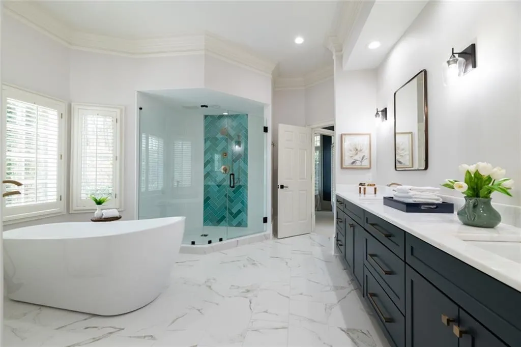 This beautifully remodeled primary bath features elegant marble countertops, a spa-like soaking tub, and a spacious glass-enclosed shower. Bright and sophisticated, it offers a luxurious retreat with high-end finishes throughout.