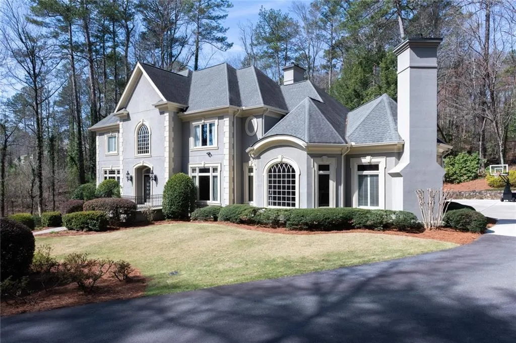 Side view highlights the home s timeless European architecture, featuring a striking turret, arched entryway, and elegant stone and stucco detailing. Surrounded by mature landscaping and set back from the drive, the residence exudes both sophistication and privacy.