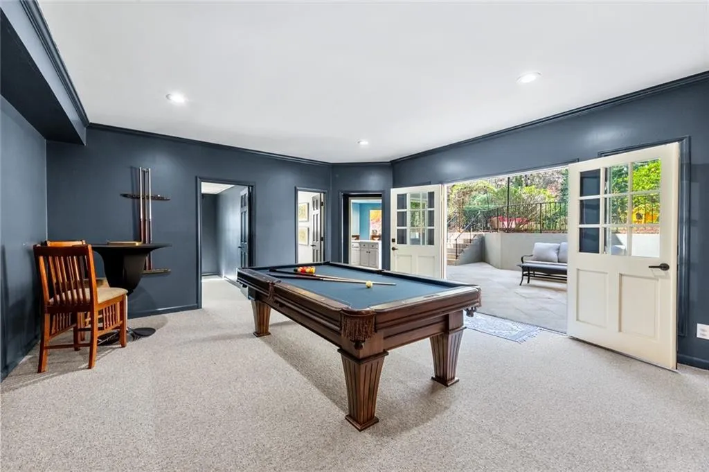 This spacious basement recreation area features a pool table and opens directly to a private patio, creating a seamless indoor-outdoor entertainment space. Large doors bring in natural light while providing easy access to the backyard and pool area.