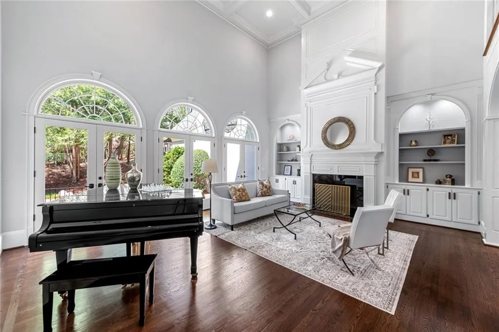 This elegant formal living room features soaring ceilings, abundant natural light, and refined finishes, creating a bright and sophisticated gathering space. French doors open to a private patio overlooking the pool, seamlessly blending indoor and outdoor living.