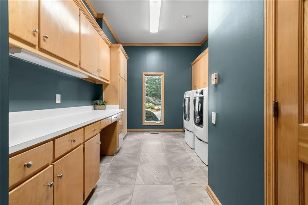 This spacious, galley-style laundry room features extensive cabinetry and a long countertop, providing abundant storage and workspace for everyday tasks. Thoughtfully designed with a full-size washer and dryer and durable flooring, it offers both functionality and a clean, modern feel. Have bath located in this area.