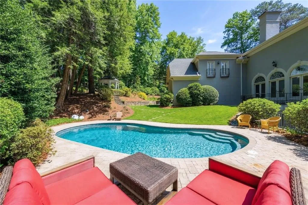 This beautifully landscaped backyard showcases a sparkling pool with scenic views extending toward the private gazebo. Surrounded by lush greenery, it offers a serene and inviting setting for outdoor relaxation and entertaining.