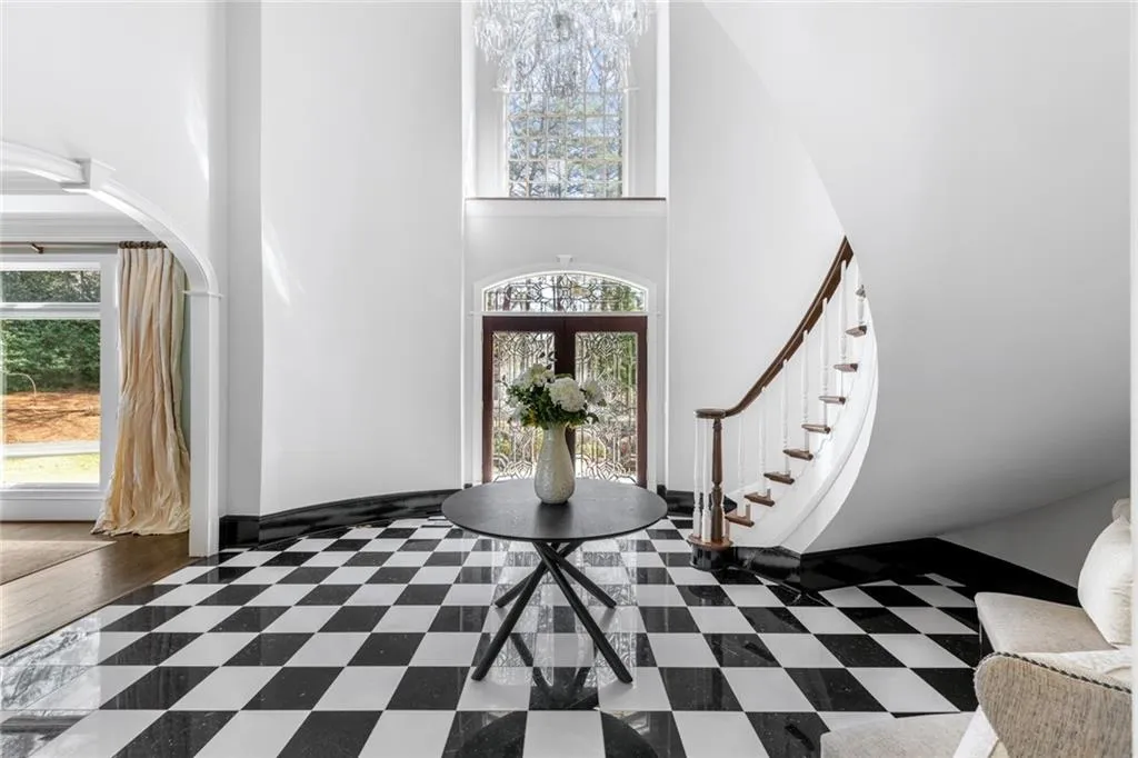A grand entrance sets the tone with a dramatic two-story foyer, highlighted by striking black-and-white marble flooring and abundant natural light. The sweeping curved staircase adds a sense of elegance and scale, creating an unforgettable first impression.