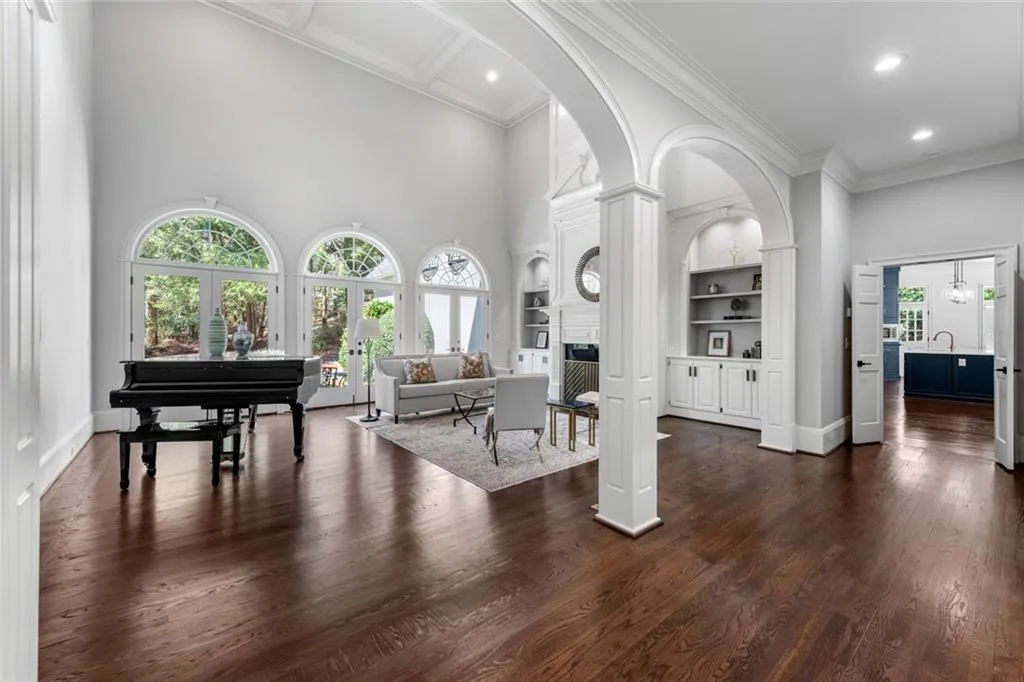 This elegant main-level formal living room features rich hardwood floors, soaring ceilings, and beautiful architectural details that create a bright, open feel. Expansive windows fill the space with natural light, enhancing its refined yet inviting atmosphere.