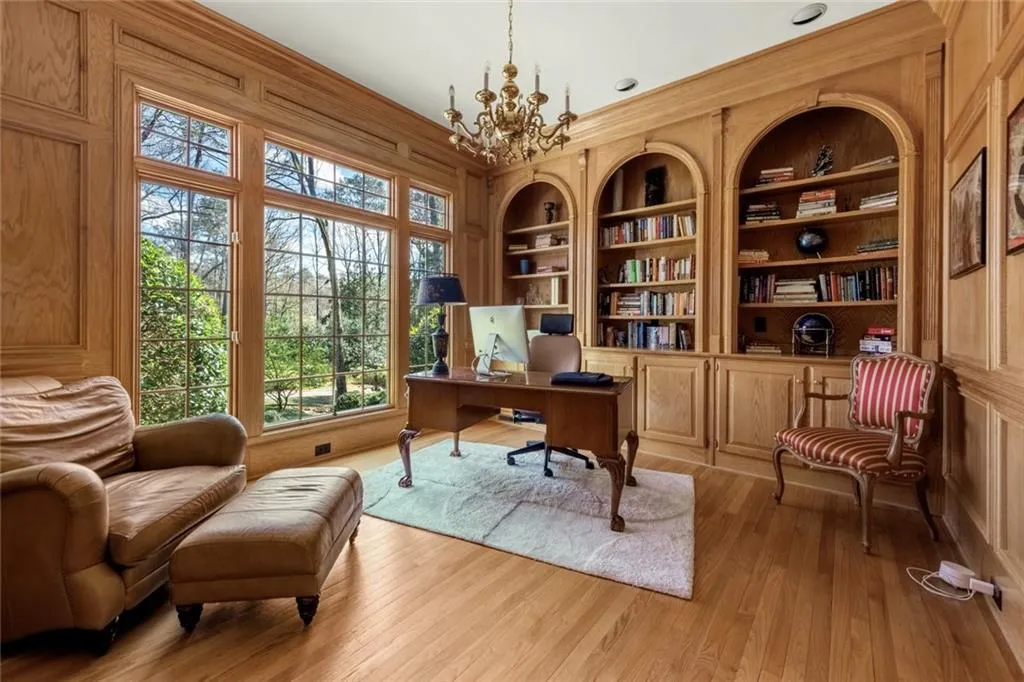 This beautifully appointed home office features rich wood paneling, custom built-in shelving, and expansive windows that fill the space with natural light. A perfect blend of elegance and functionality, it offers a warm and inspiring setting for work or study.