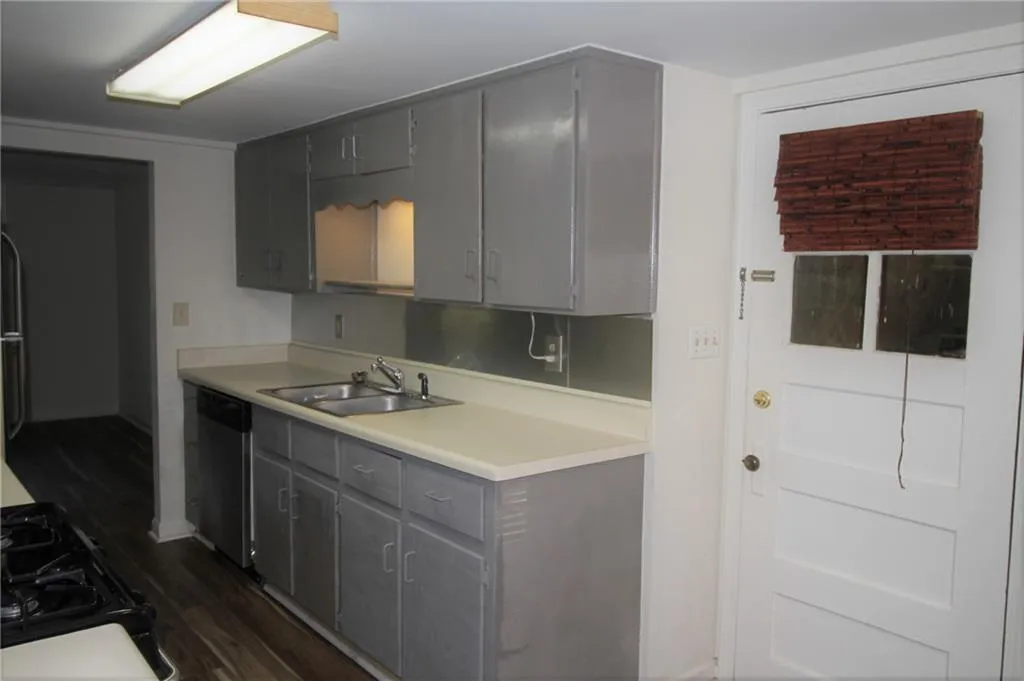 Kitchen featuring light countertops, gray cabinets, dark wood-style flooring, stainless steel dishwasher, and a sink