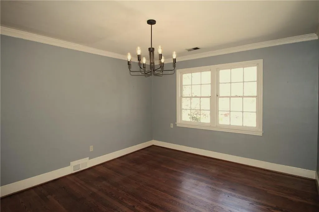Empty room with an inviting chandelier, crown molding, baseboards, and visible vents
