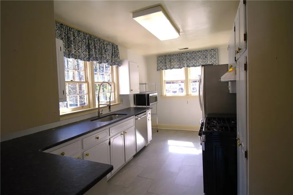 Kitchen featuring white cabinets, stainless steel appliances, dark countertops, a sink, and ventilation hood