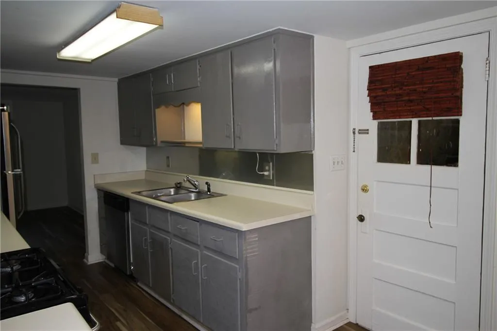 Kitchen with dark wood-style flooring, light countertops, a sink, gray cabinets, and stainless steel dishwasher