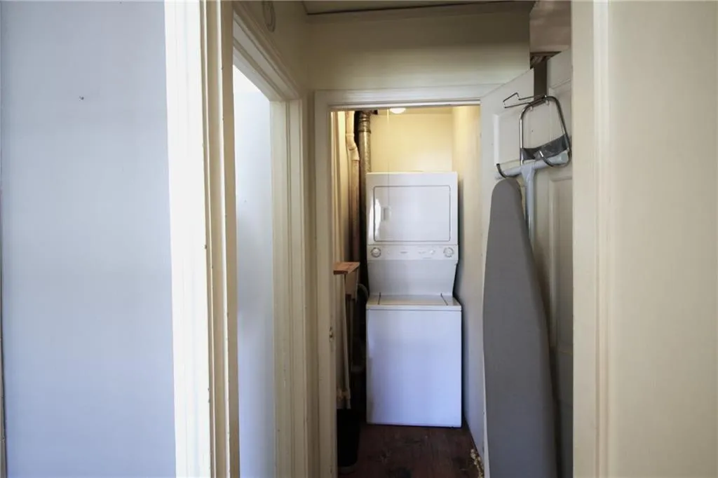 Washroom featuring stacked washer and clothes dryer, dark wood-type flooring, and laundry area