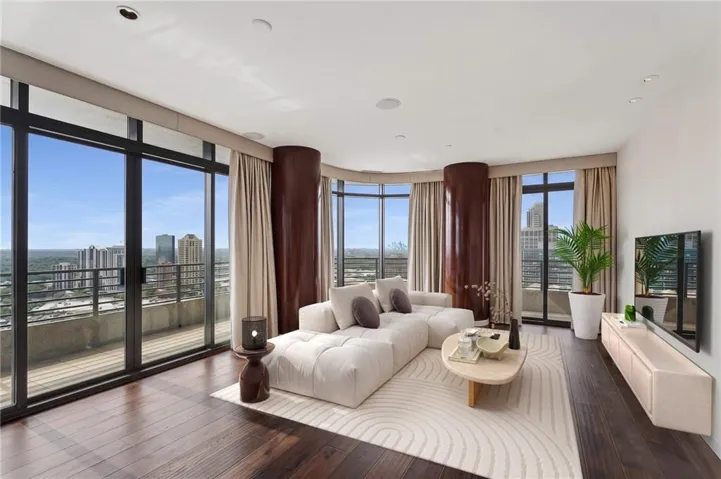 Expansive living area featuring floor-to-ceiling windows, dark wood-finish flooring, a private outdoor balcony, recessed lighting, and a neutral color palette