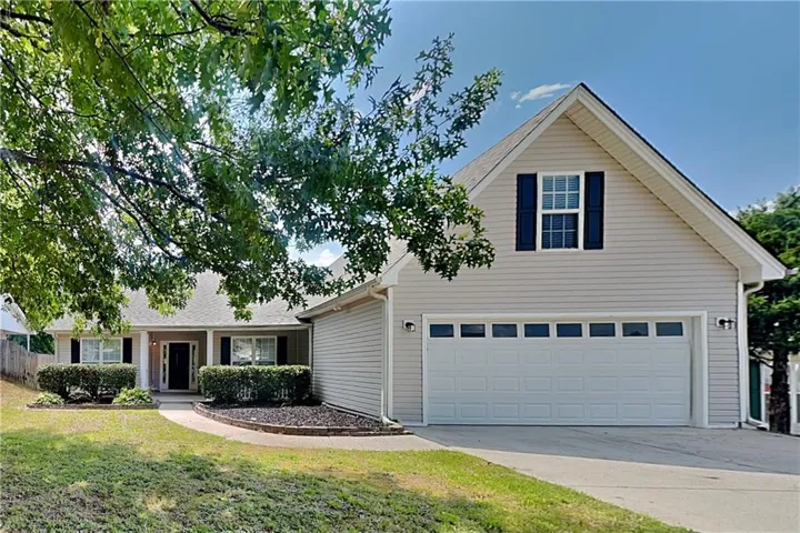 Expansive front yard with mature trees, established landscaping, and a paved driveway leading to a two-car garage with transom windows