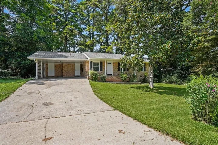 Brick facade featuring a carport, white front door, and mature trees