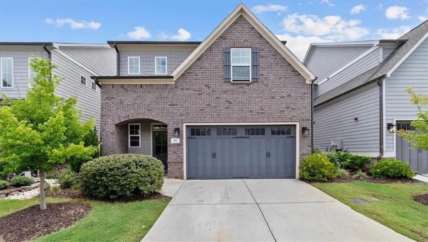 Brick and siding exterior with an arched entry, a two-car garage, and mature landscaping